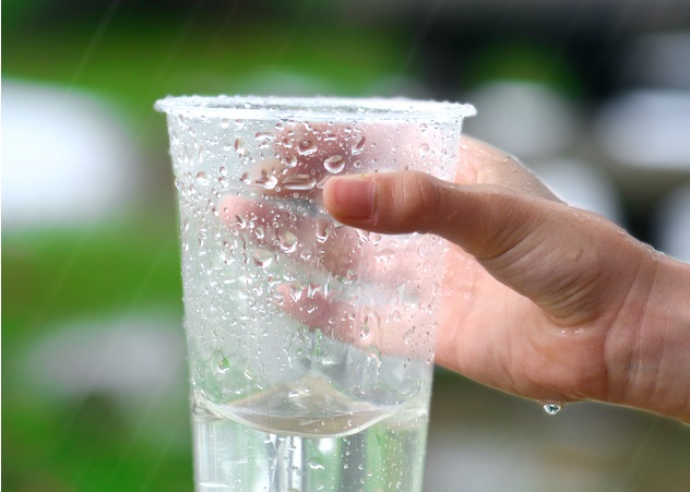 Hand of a child holding a plastic cup collecting rain water.